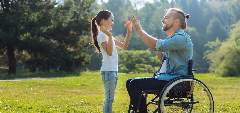 man in a wheel chair playing with his daughter outside in the sun