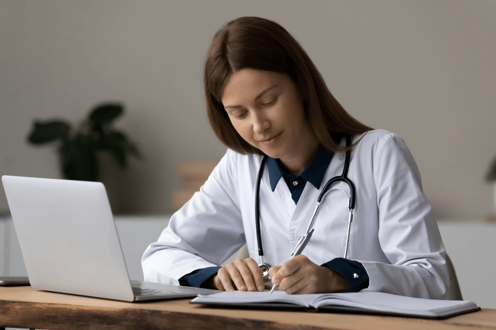 a doctor in a white coat working on her labtop at her desk